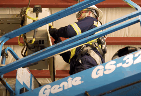 Caucasian male is working on digital equipment as a Service Technician, standing on a Mobile Elevated Platform, aka MEWP.